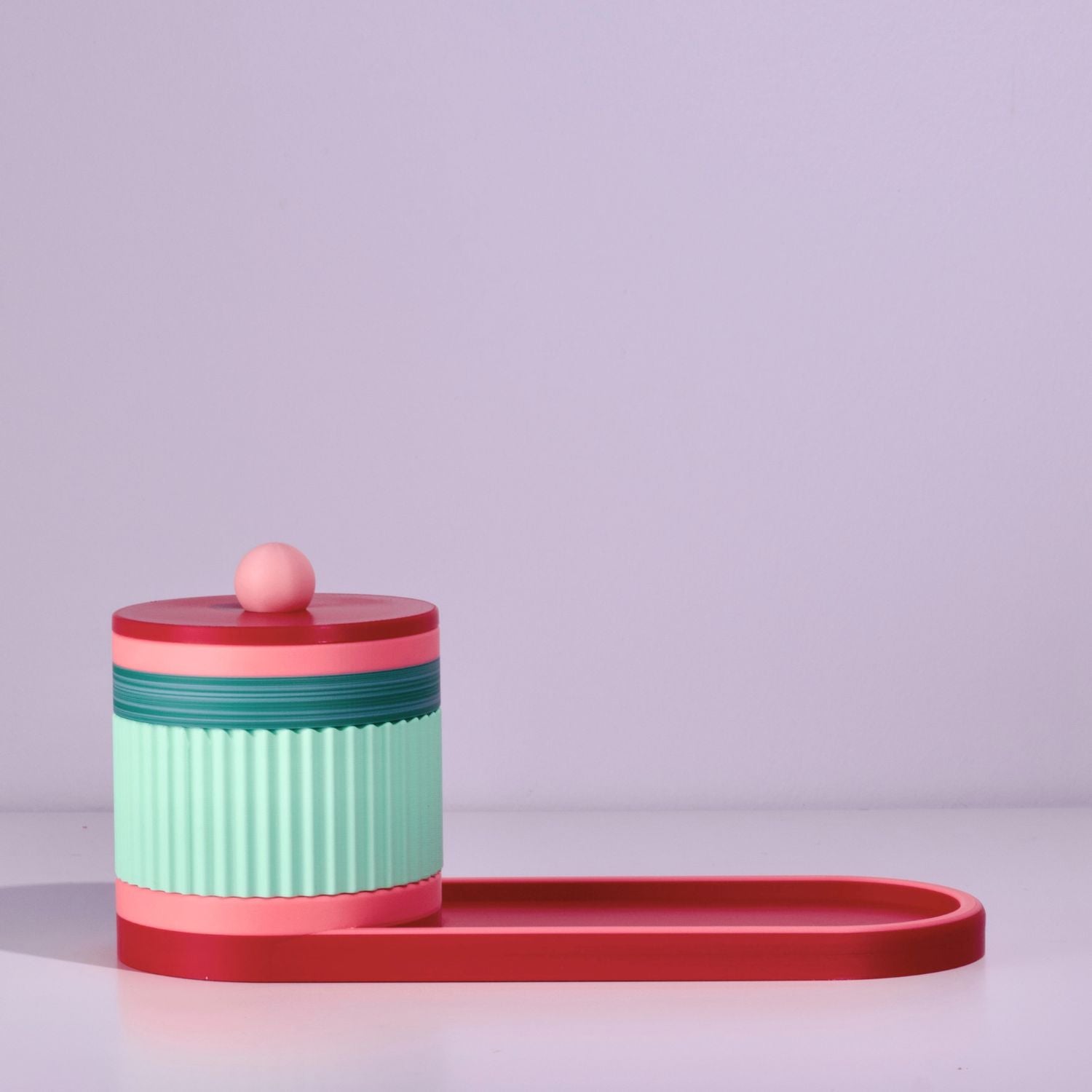 Colorful cylindrical container with a lid and tray on a light grey background